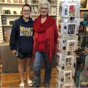 Pat and her granddaughter pose next to a display of cards Pat designed.